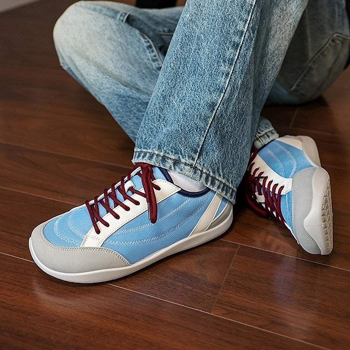 SNK AeroStitch Trainer Sky Blue on feet, seated on a wooden floor